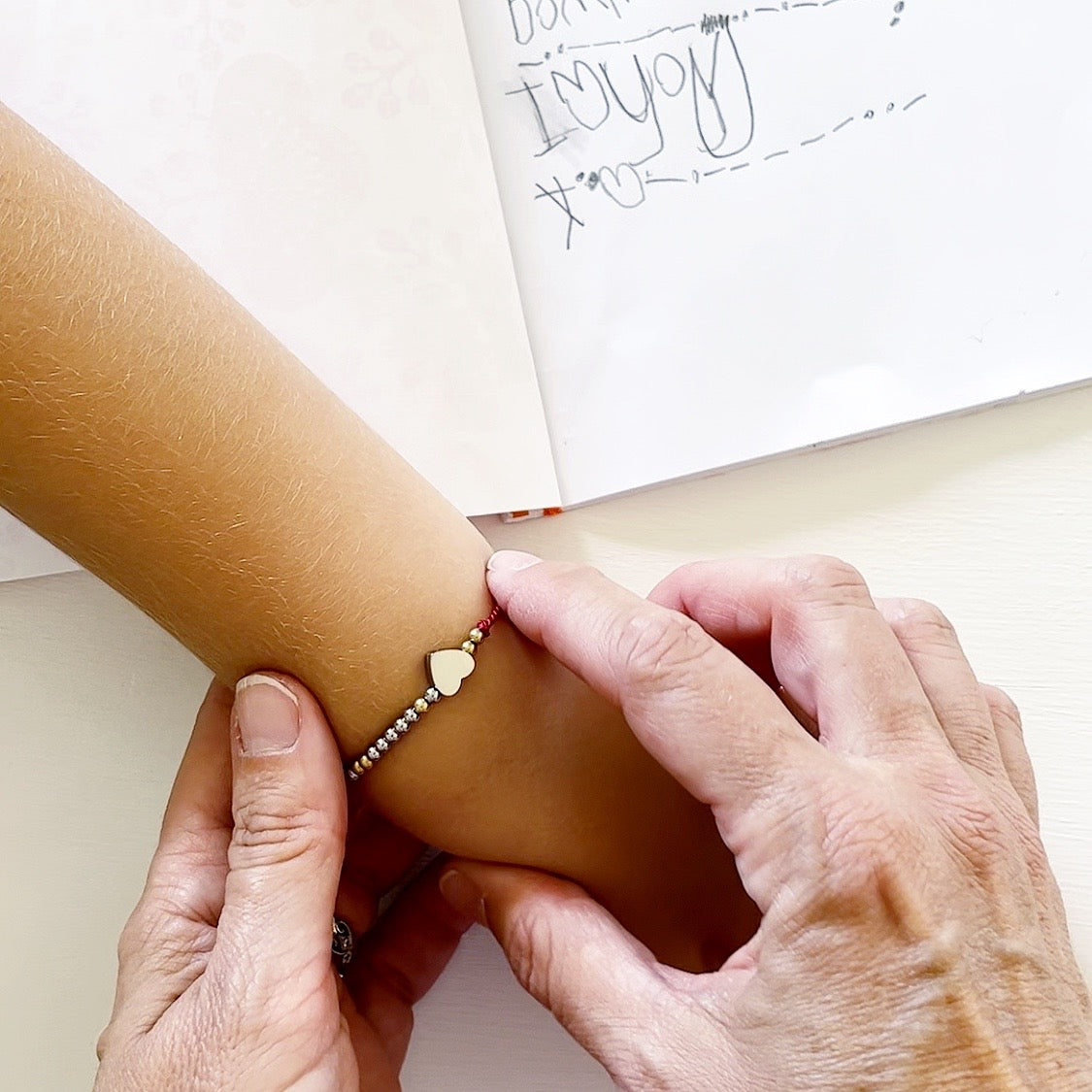 Woman putting an 'I love you' Morse Code and charm beaded bracelet on a child