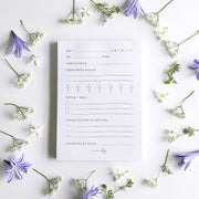 White self-care notepad with lilac text and flowers.