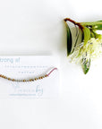 Strong AF Morse code beaded bracelet on pink cord on a white card with blue text