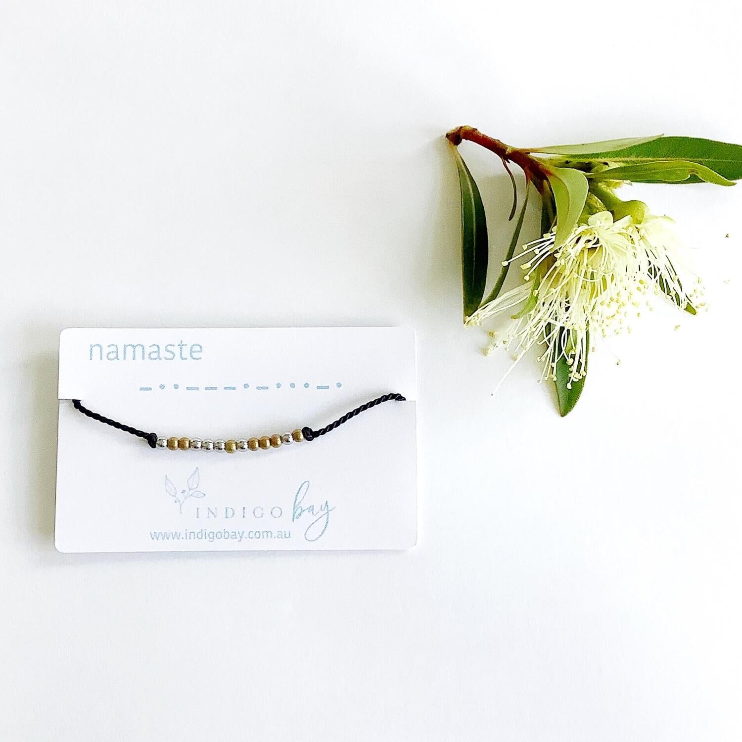 Namaste Morse code beaded bracelet on black cord on a white card with blue text
