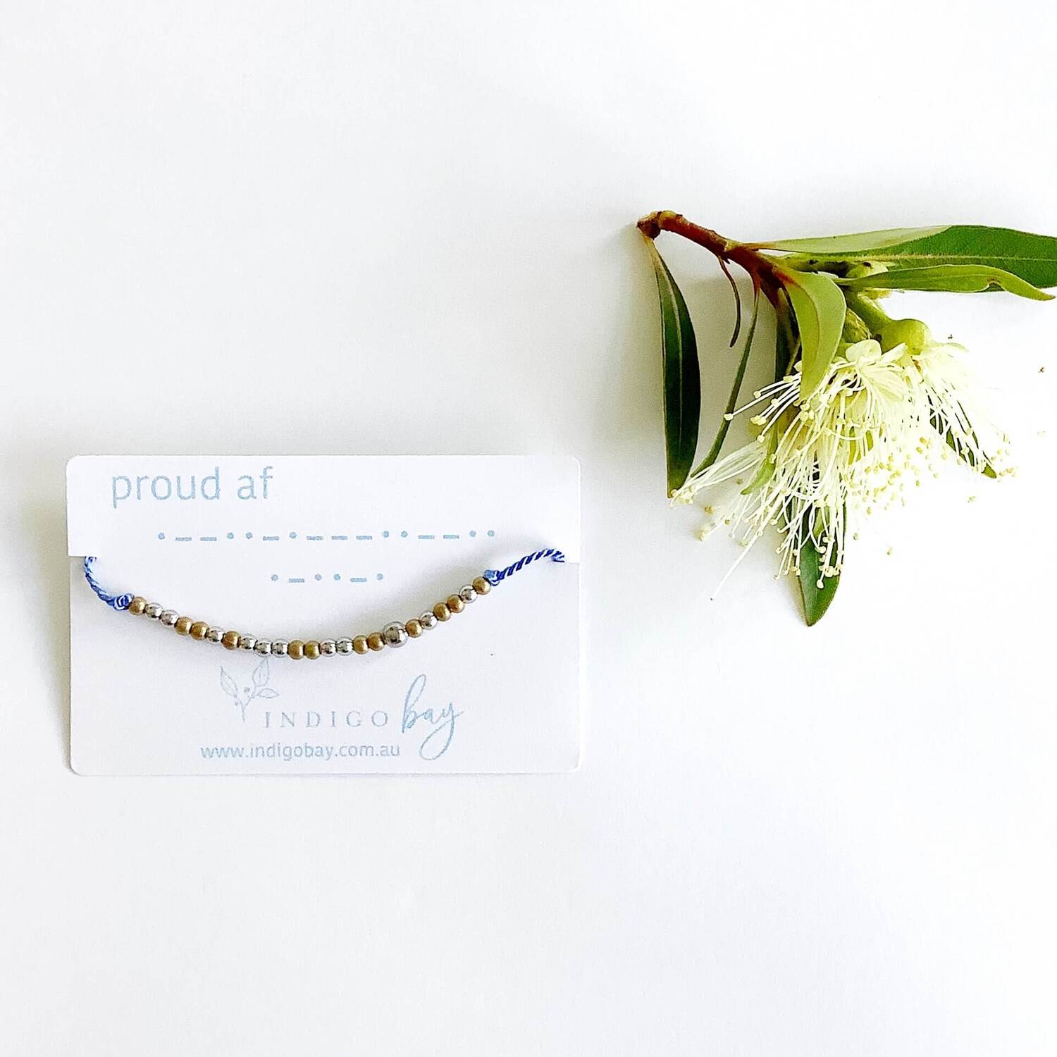 Proud AF Morse code beaded bracelet on light blue cord on a white card with blue text