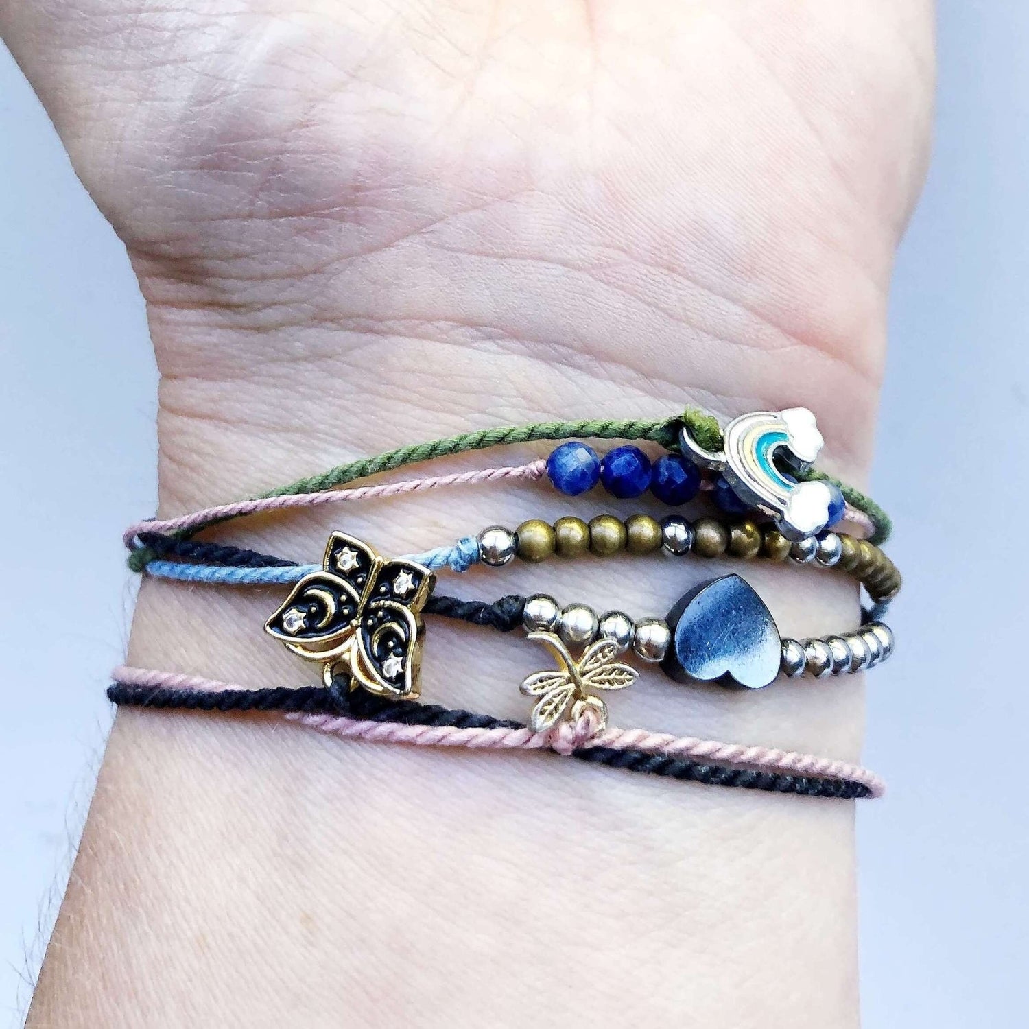 6 beaded and charm bracelets including a black butterfly, black heart, gold dragonfly, and rainbow on a woman&#39;s wrist