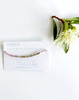 Magical Morse code beaded bracelet on pink cord on a white card with blue text